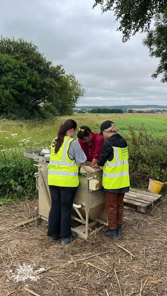 Archaeologists, two in hi vis vests, crowd around an environmental wet sieving tank