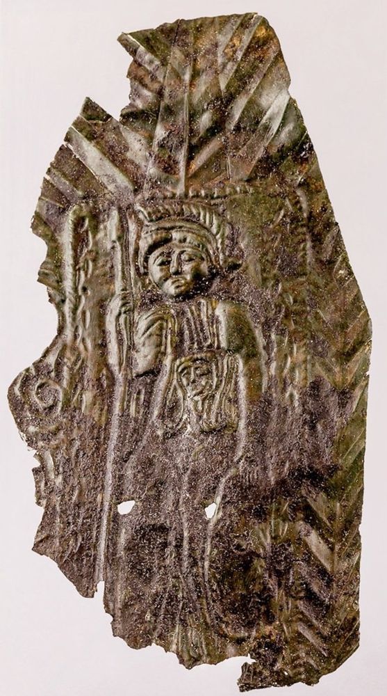 Thin copper alloy sheet with a lightly hammered image of a female figure wearing an archaic Greek helmet and holding a spear in her right hand, the left resting on a shield