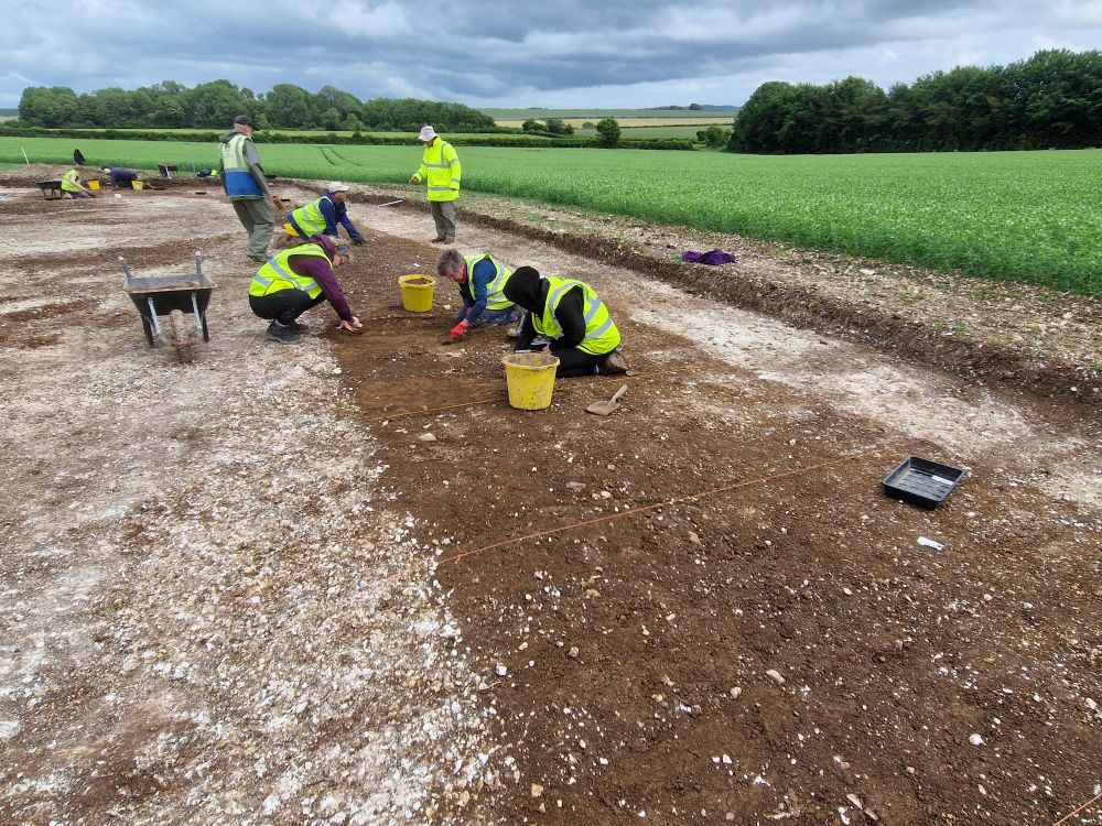 Archaeologists in Hi Viz excavating sections across a dark soil-filled linear ditch feature cut into chalk