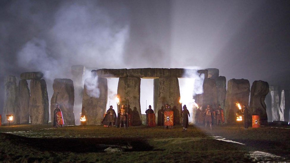 Stonehenge at night with a rising fog and interior light source guarded by Autons (or Nestene duplicates if you prefer) dressed as Roman legionaries