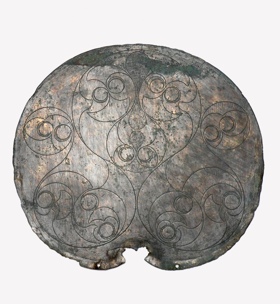 The circular backplate of a copper alloy mirror incised with swirling La Tene style (Celtic) decoration over 2 thousand years ago in the late Iron Age 
