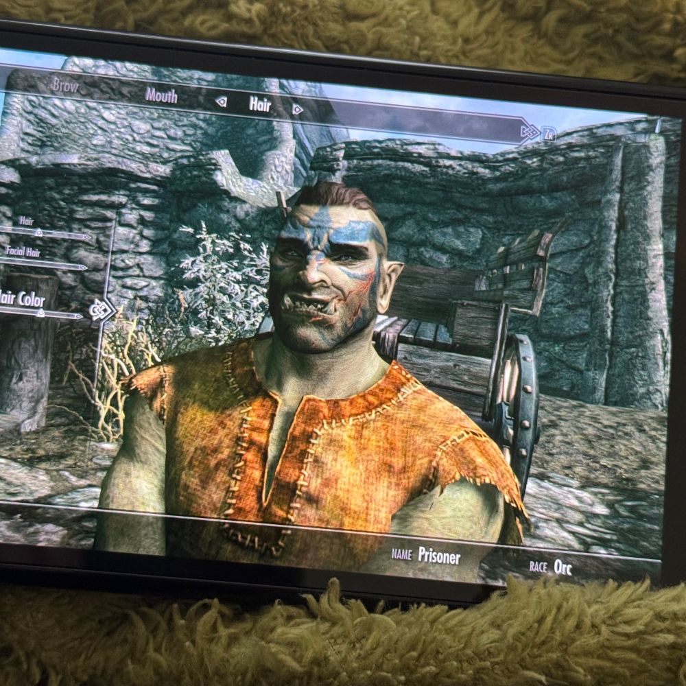 a switch showing a character creation screen for the game The Elder Scrolls V: Skyrim. the character on screen is an orc with blue face paint 