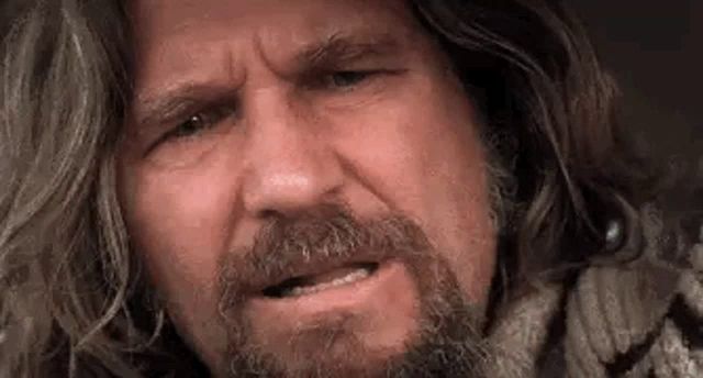 a close up of a man with long hair and a beard making a face .