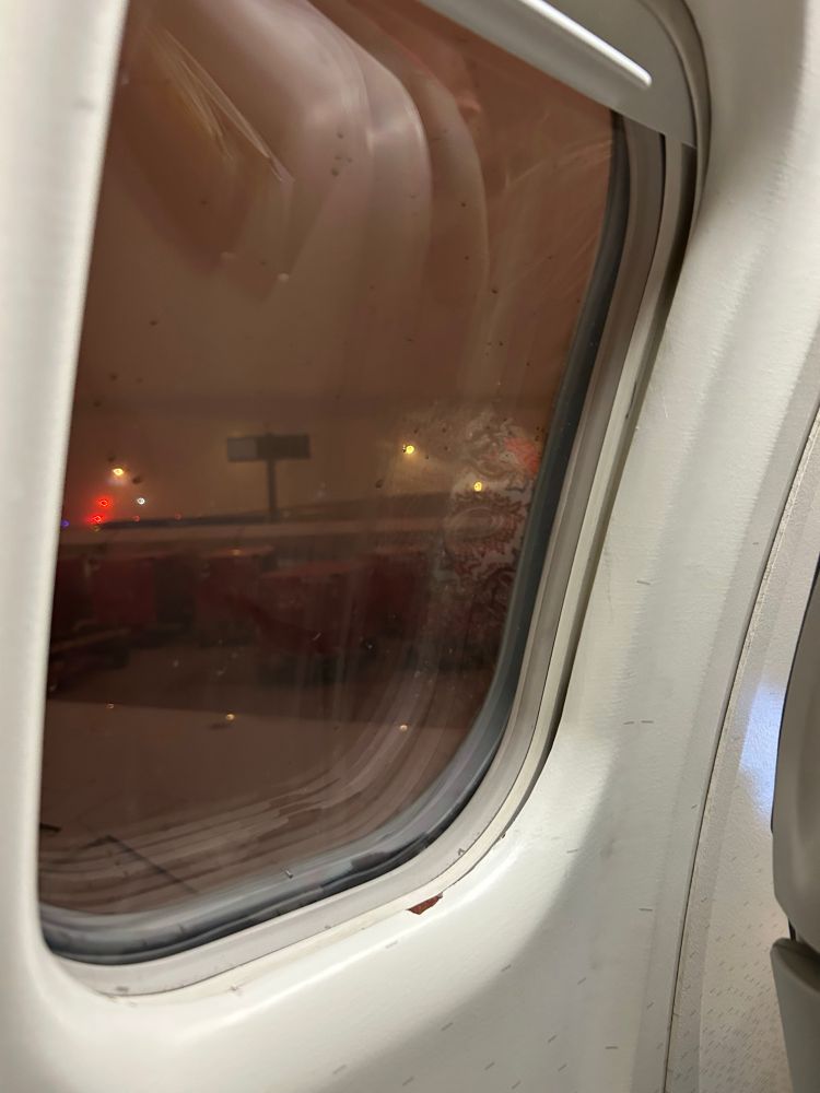 View out the window of a passenger jet on the runway, a gigantic dust storm moves in. It looks like night but it is the storm that has blotted out the sun. 