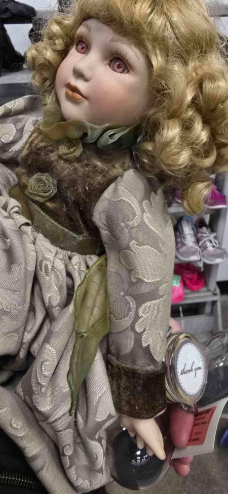Old porcelain doll with pink eyes and a sickly green dress
