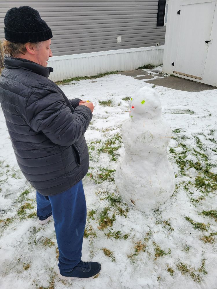 Person in black coat and hat with blue sweats putting candy into a snowman face
