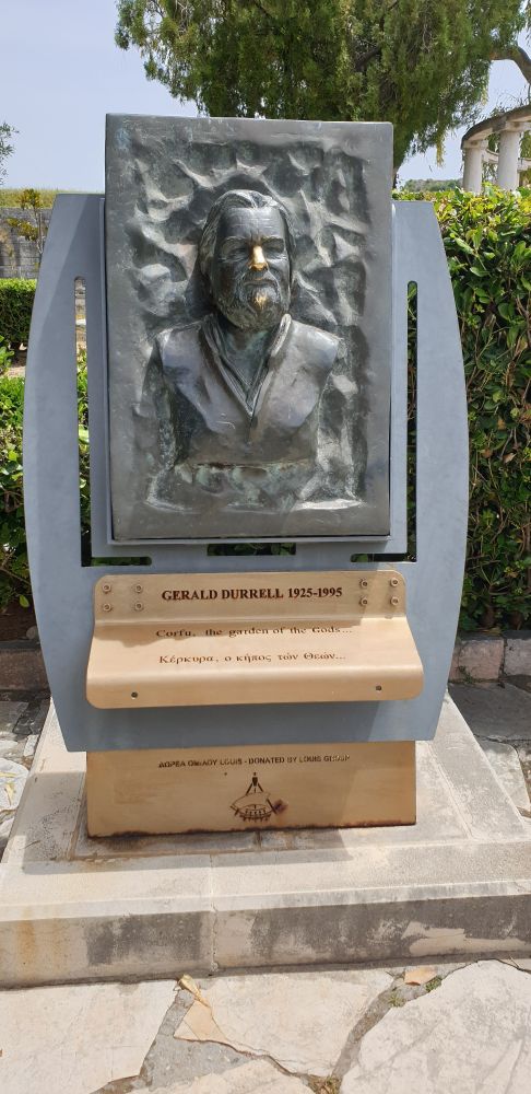 Bronze sculpture of Gerald Durrell. Rectangular relief about 1 meter tall on a stand mounted on marble plinth. Green hedge behind.