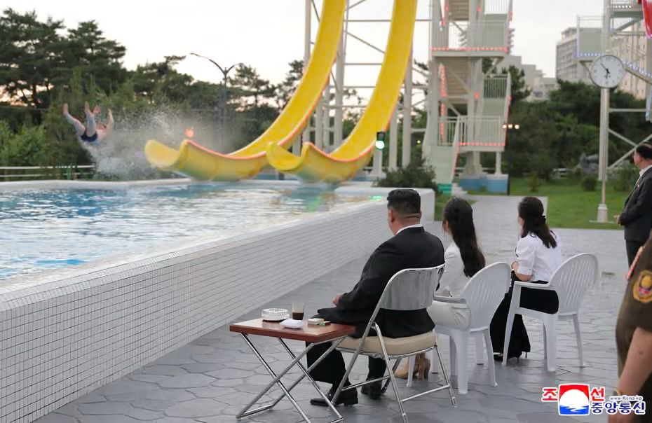 Kim Jong Un watching a bloke go down a slide, with a black coffee and ciggies. 