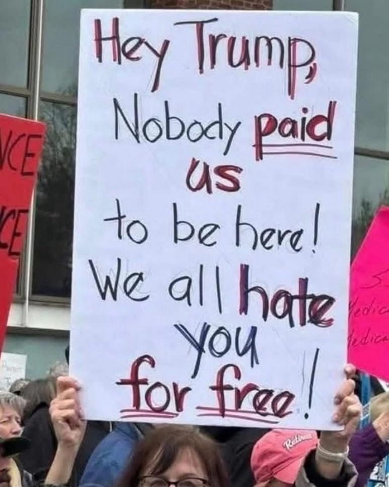 A woman holds up at a homemade protest sign with bold handwritten letters at the No Kings Day protest in America 🇺🇸 on June 14, 2025. The sign reads: 

Hey Trump, Nobody paid us
to be here!

We all hate
You
for free!