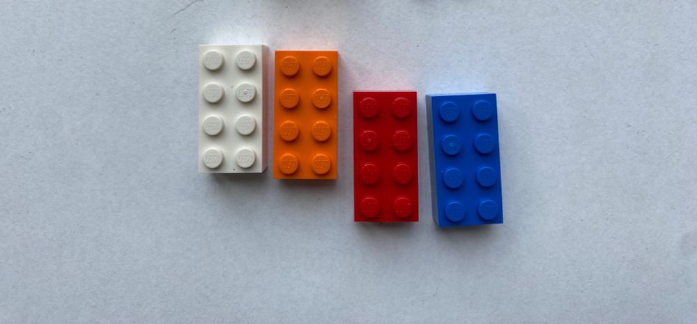 Bild von 4 Legosteinen in den Farben, weiss, rot, orange und blau.