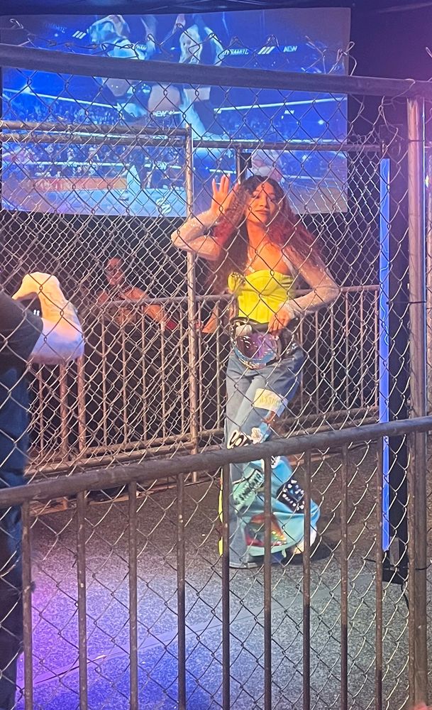 professional wrestler mercedes moné standing in the mpx entrance ramp at mpx who runs the world? she has one hand on her belt and one cupping her ear and she looks amazing 