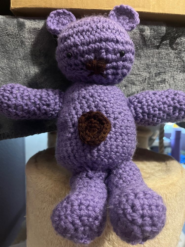 purple crocheted bear with a brown belly button brown nose and mouth and black safety eyes