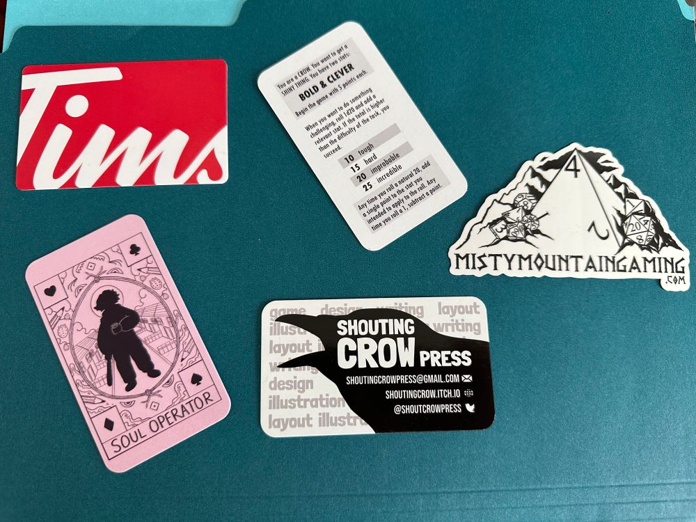 A Tim Hortons gift card, business cards for Soul Operator and Shouting Crow Press, And a sticker for Misty Mountain Gaming (dot com). 

On the other side of the Shouting Crow Press is a small TTRPG game. 

You are a CROW. You went to get a SHINY THING. You have two stats: BOLD & CLEVER. Begin the gome with 5 points each.

When you want to do something challenging, roll 1d20 and add a relevant stat. If the total is higher then the dificulty of the task, you succeed.

10, tough.
15, hard.
20, improbable.
25, incredible.

Any time you roll a natural 20, add a single point to the stat you intended to apply to the roll. Any time you roll a 1, subtract a point.