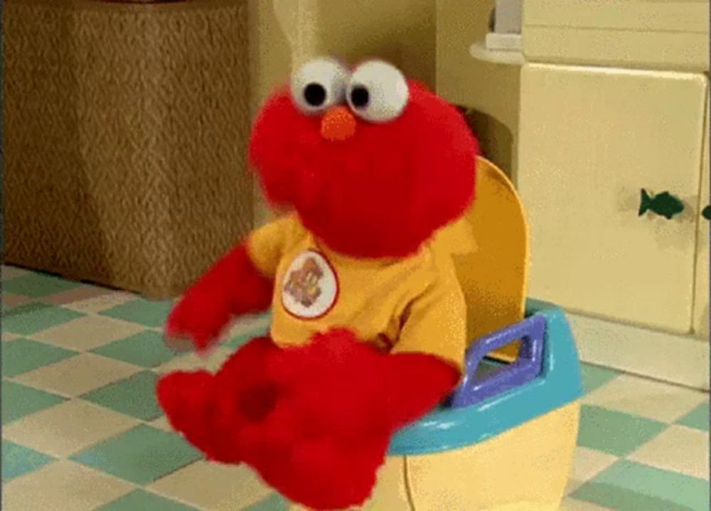 elmo is sitting on a potty wearing a yellow shirt with a bear on it .