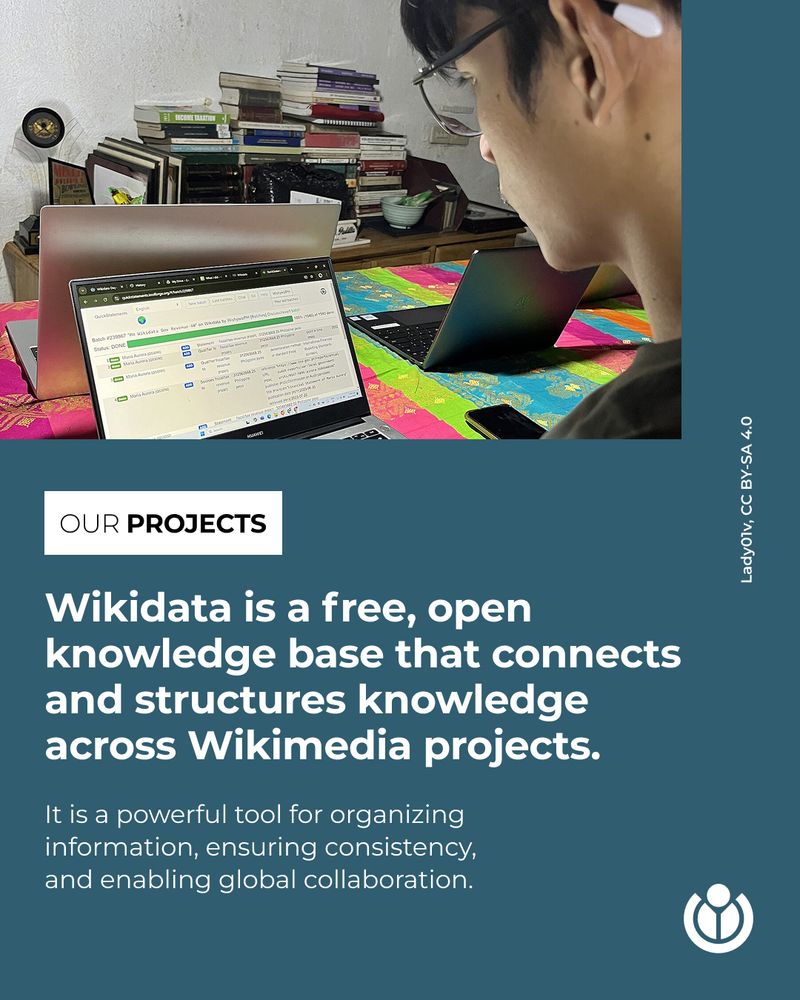 A person wearing glasses and wireless earbuds is typing on a laptop at a colorful table covered in fabric. Behind them is a cluttered shelf stacked with books and various items in a room with plain, white walls. Text says: Wikidata is a free, open knowledge base that connects and structures knowledge across Wikimedia projects. It is a powerful tool for organizing information, ensuring consistency, and enabling global collaboration.