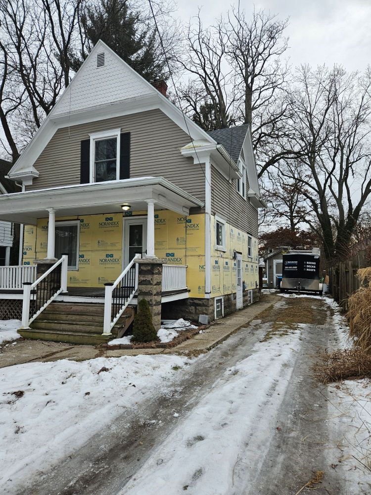 A beige house with peeling paint, covered on its lower half by those foam panels they nail to walls before putting new siding on. The photo is taken from the driveway, which is full of dirty refrozen rutted slush.