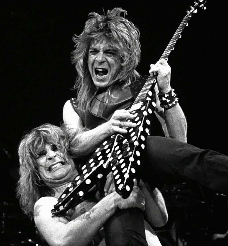 An iconic photo of Ozzie Osborne hoisting Randy Rhodes in the air while he plays a pokadot flying-V guitar. 