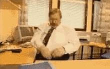 A man sat at a desk, throws papers around up in the air and crosses his arms.