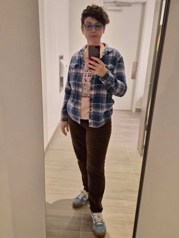 Flux wearing a blue and pink flannel over a pink shirt reading Have a Killer Day, brown cords, light blue Adidas shoes.