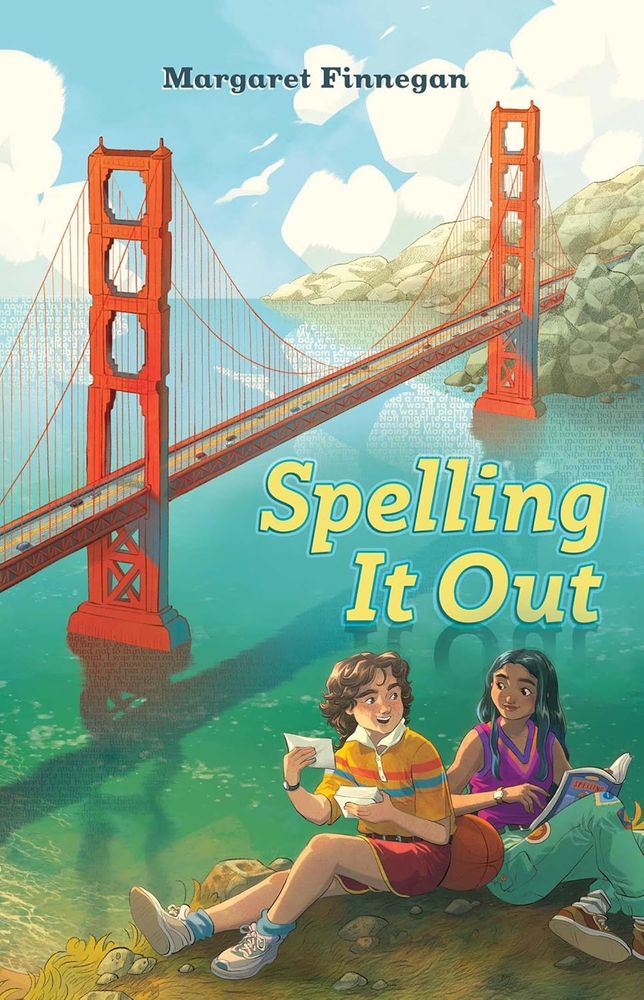 Illustrated book cover for Spelling It Out by Margaret Finnegan. The background features the iconic Golden Gate Bridge in San Francisco, spanning across water with hills in the distance. The bridge and water are overlaid with faint, transparent text. In the foreground, two smiling girls sit on grass near the water. One wears a striped shirt and shorts, holding papers and a basketball. The other wears a purple top and teal pants, reading a book or magazine titled “Spelling.” The atmosphere is bright and cheerful, suggesting a middle-grade or young adult story.