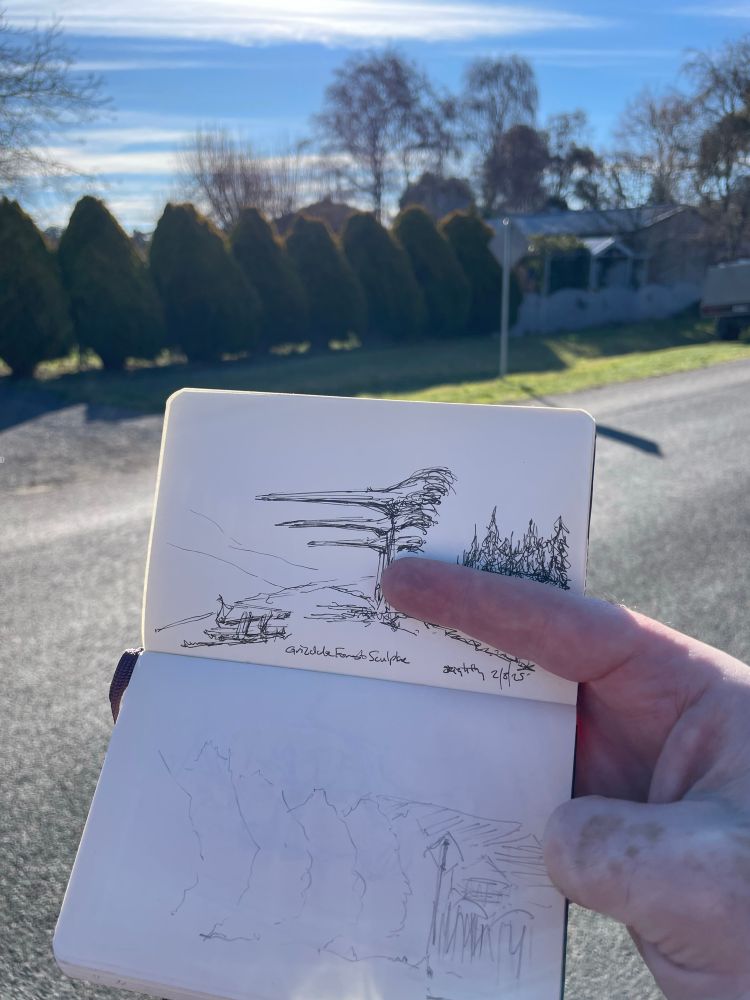 Photo of the drawing and scene together, with the notebook held up in front of the scene. Yesterday’s drawing is visible in the book. 