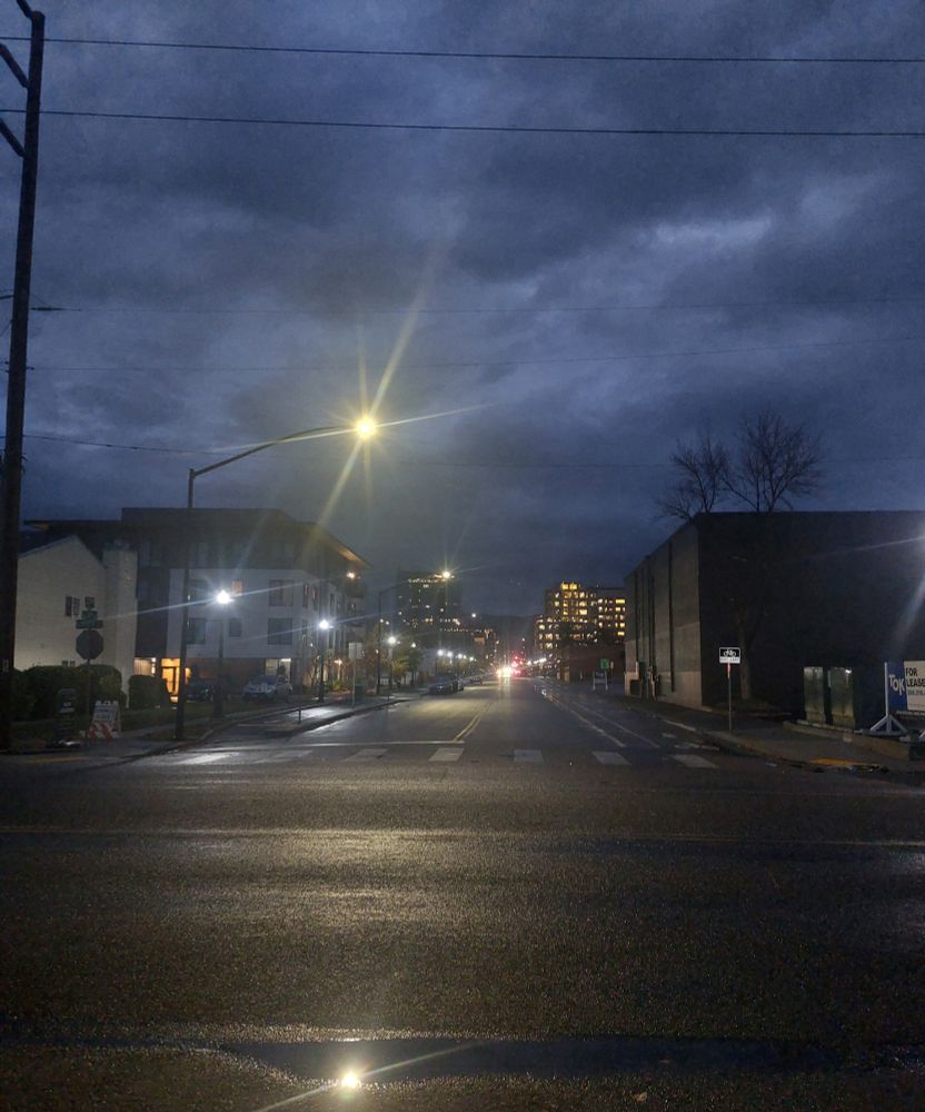 A photo of a wet city street in still-dark early morning.