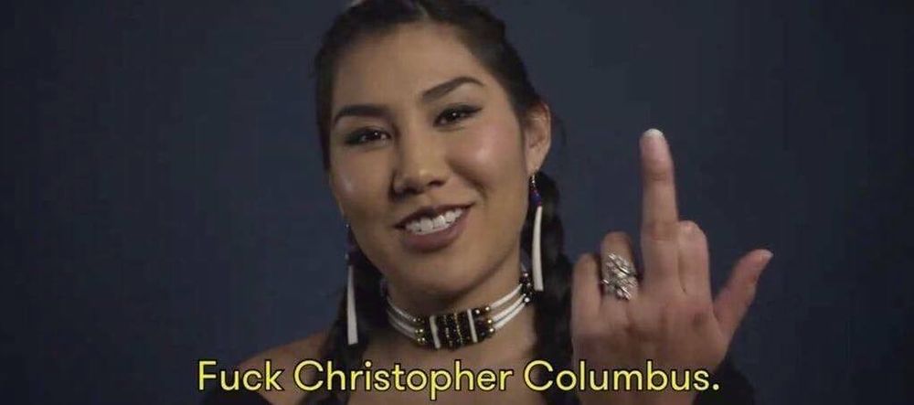 well-known still frame of an Indigenous woman with a raised middle finger, and the subtitle "Fuck Christopher Columbus".