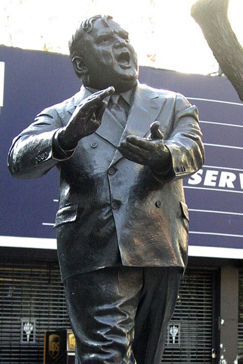 Picture of a statue of Fiorello LaGuardia strolling with his hands almost clasped. 