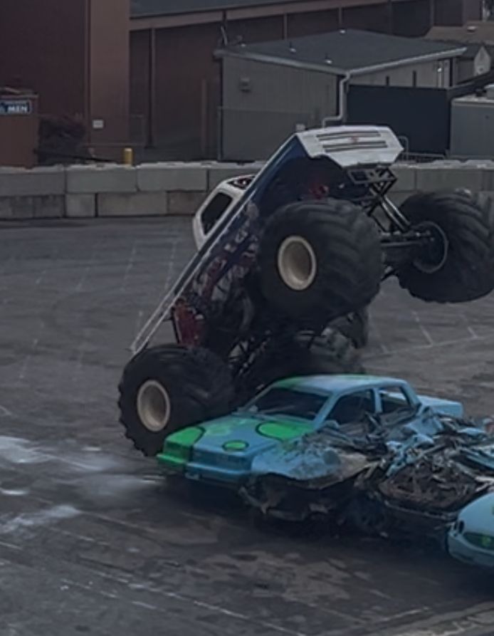 A truck with giant wheels running over a line of cars. 