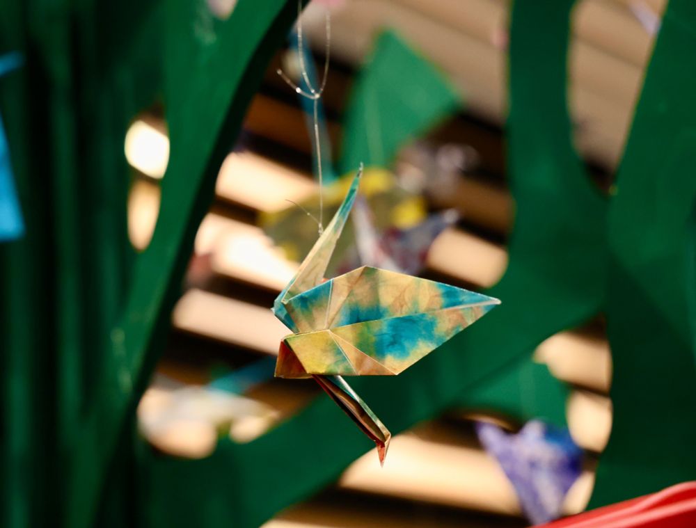 An origami crane decoration hanging from a green wooden tree.