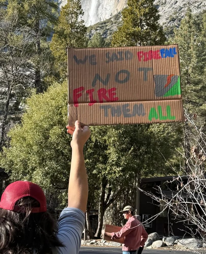 A colorful sign is held up that reads "We said Firefall, Not Fire them All" 