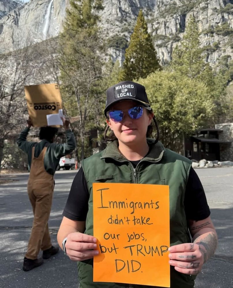 A person holds a sign that says "Immigrants didn't take our jobs, but Trump did" 