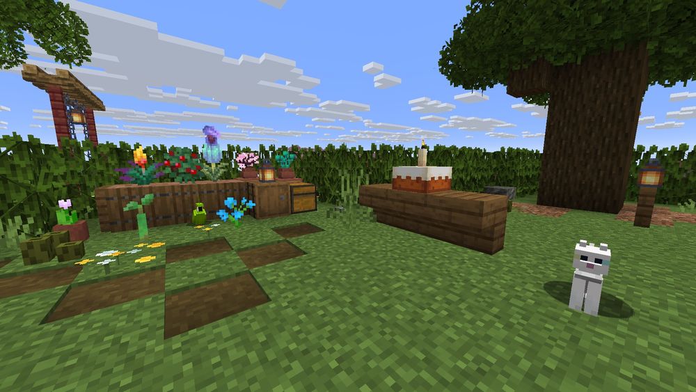 Minecraft screenshot of a small farm stand of plants to the left. There’s a green parrot in front of it. To the right is a small table with a cake with a candle in it. There’s a white cat on the right. 