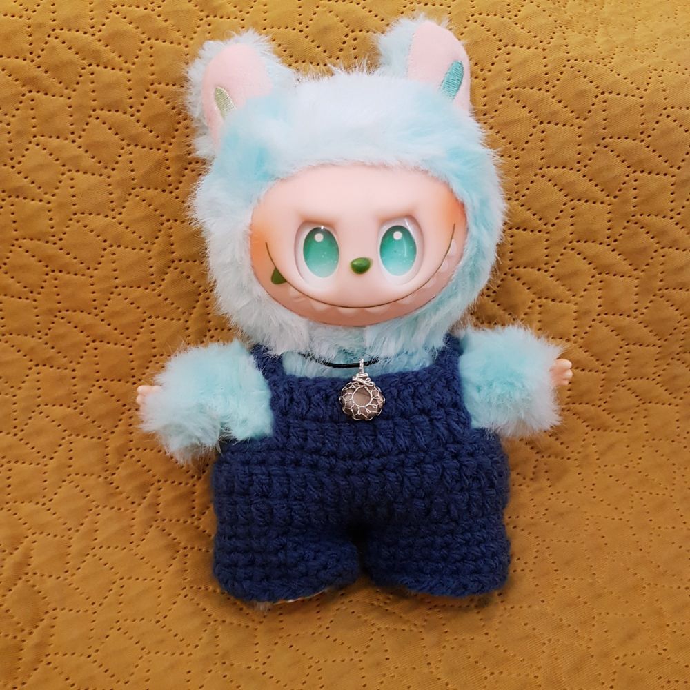 Green fluffy demon doll in blue overalls, wearing a small golden labradorite drop necklace.