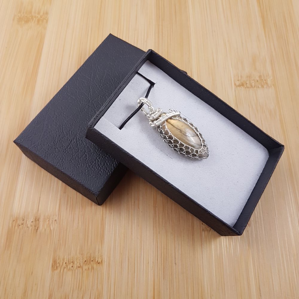 Small golden drop pendant netted in silver wire, sitting in black and white gift box.