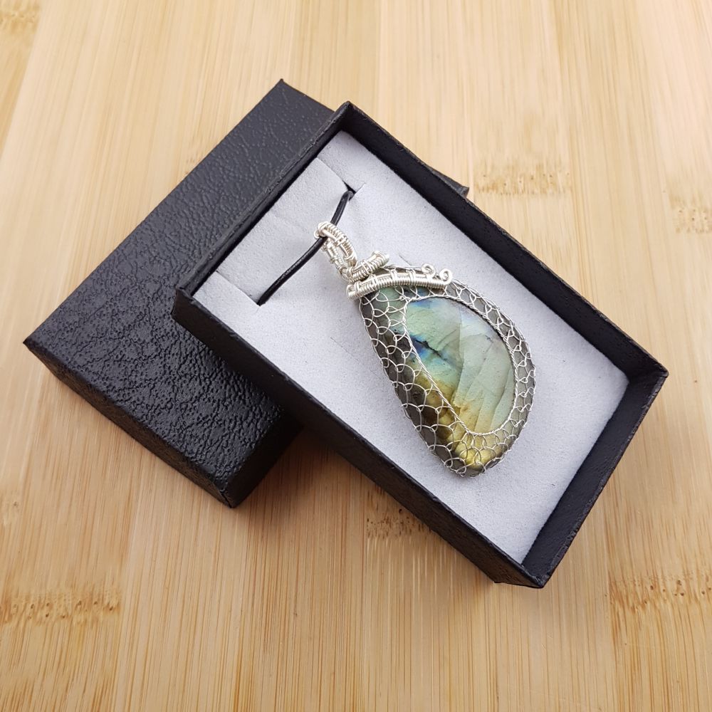 Angular green and gold labradorite pendant netted in silver wire, sitting in black and white gift box.