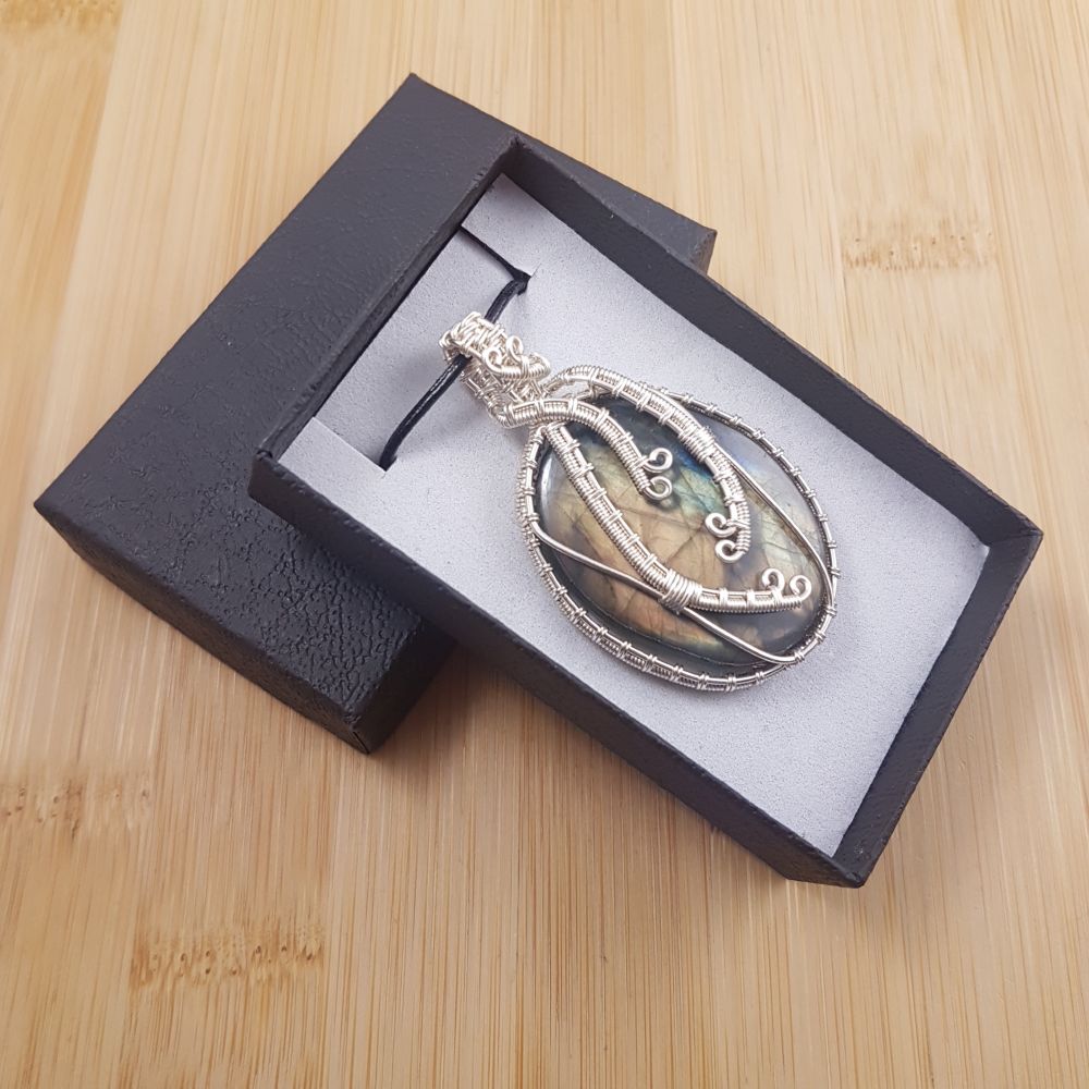 Large golden oval labradorite pendant wrapped in wavy silver wire, sitting in black and white gift box.
