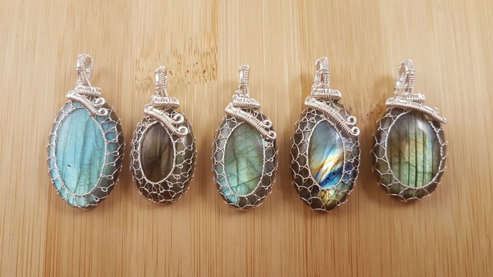 Row of 5 oval labradorite pendants netted in silver wire, all shining in greens, blues, and gold. 