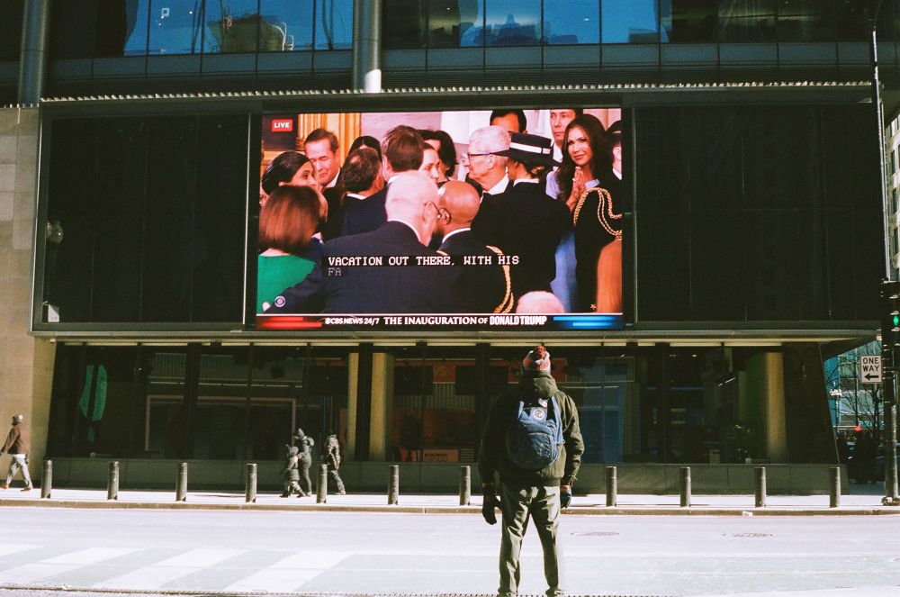 A man in a Chicago Bears hat watching a large screen showing the inauguration events