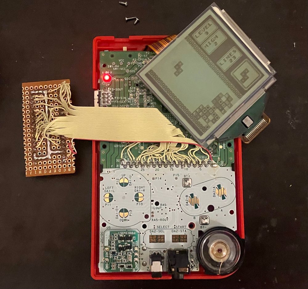 a red gameboy pocket, partially disassembled, played tetris. a ribbon cable connects perfboard to the motherboard 