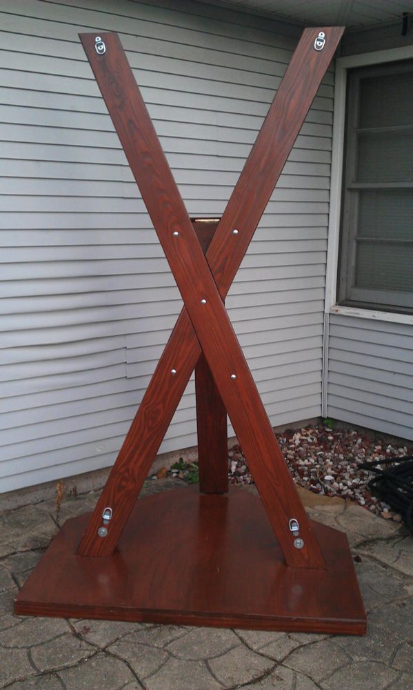 A roughly person-height wooden cross, pictured in front of a house. roughly the shape of a twitter logo. There are metal fixtures at each corner of the... logo.