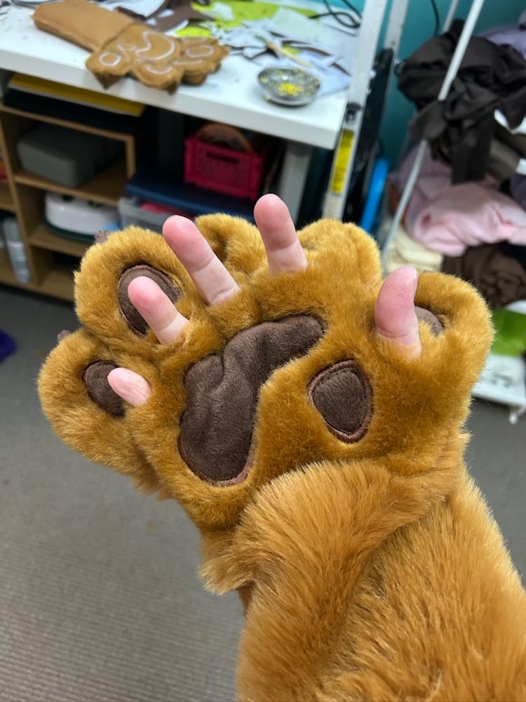 a bear fursuit paw with human fingers poking out below the paw pads