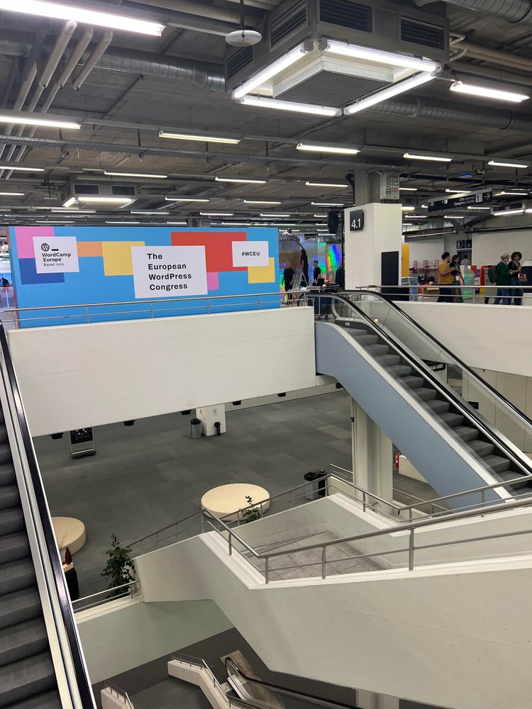 Multiple escalators with a giant blue „The European WordPress Conference“ banner behind them.