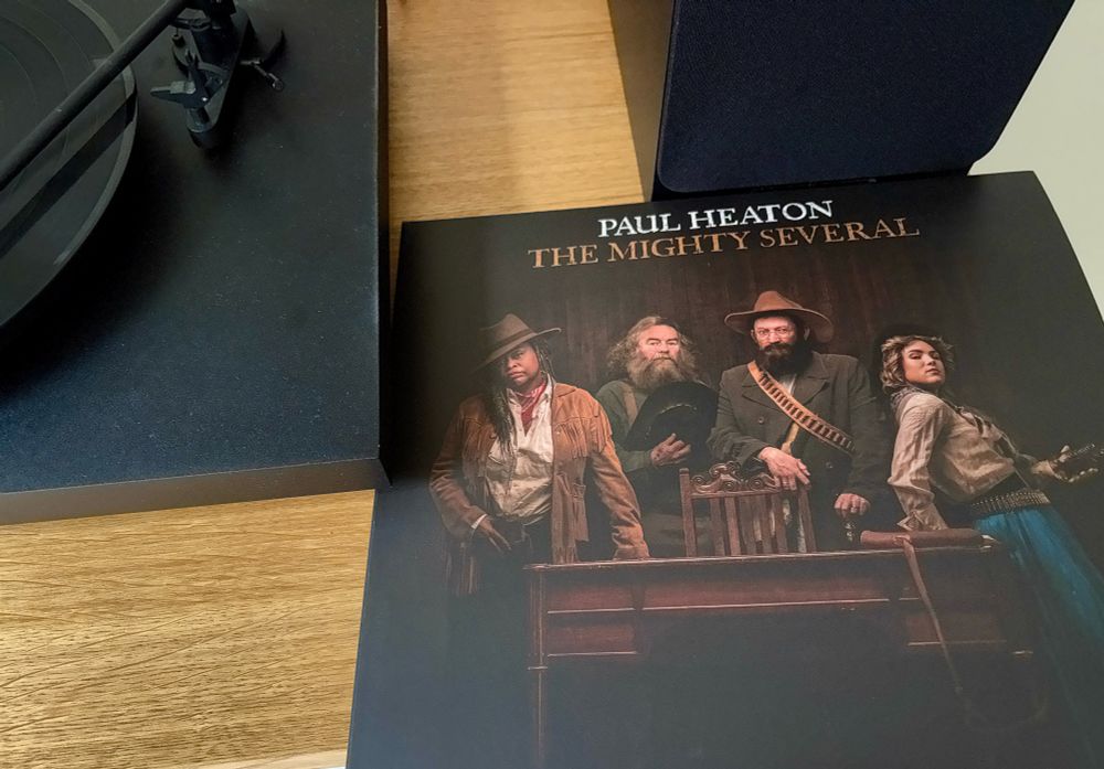 Album cover from the new Paul Heaton album, The Might Several. The cover shows four band members in frontier or western style appearance gathered around a desk looking straight into the camera, 