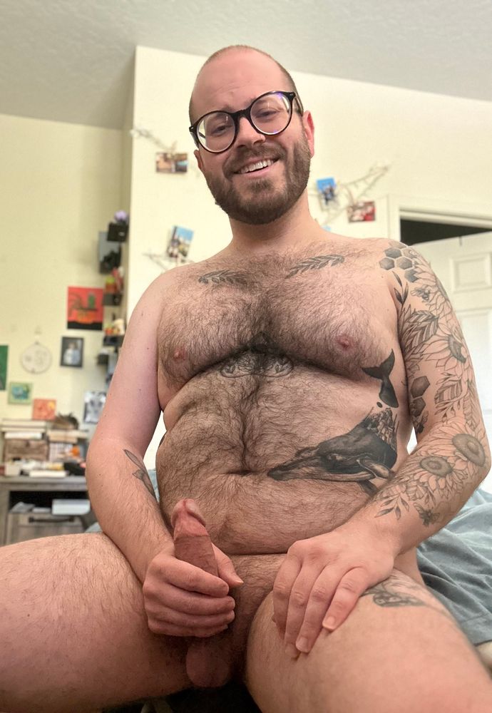 Nude hairy fellow smiling and holding erection that is leaking precum