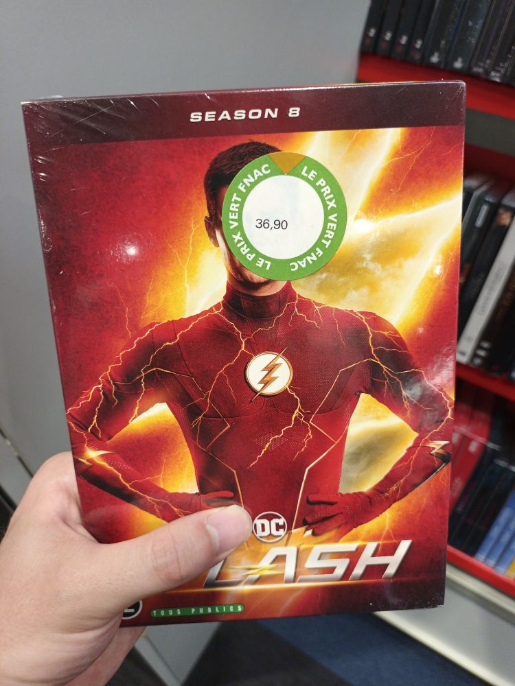 A hand holding the DvD case for "the flash" by DC, where it looks like his face was deliberately covered with the price tag.