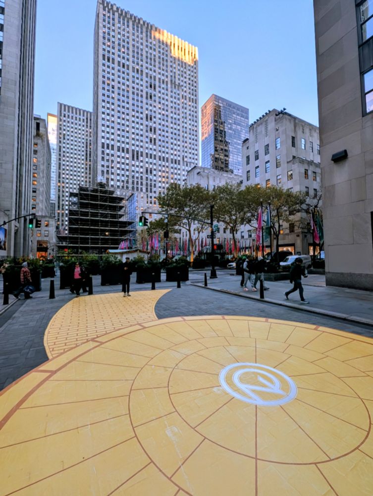 Yellow brick road painted on a street, with Rockefeller Center in the background