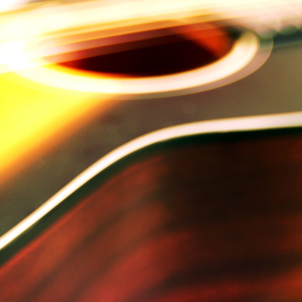 A square, colorful, and somewhat blurry photograph of a small acoustic guitar with a sunburst finish. The body, waist, strings, bottom of the neck, and sound hole are visible.