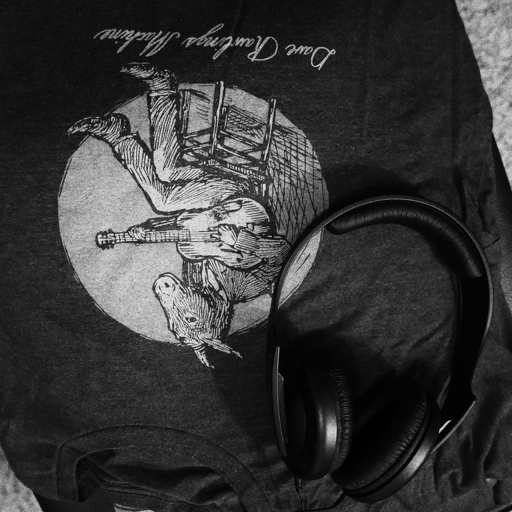 A square black and white photograph of set of Sennheiser HD202 headphones resting on top of a Dave Rawlings Machine t-shirt.