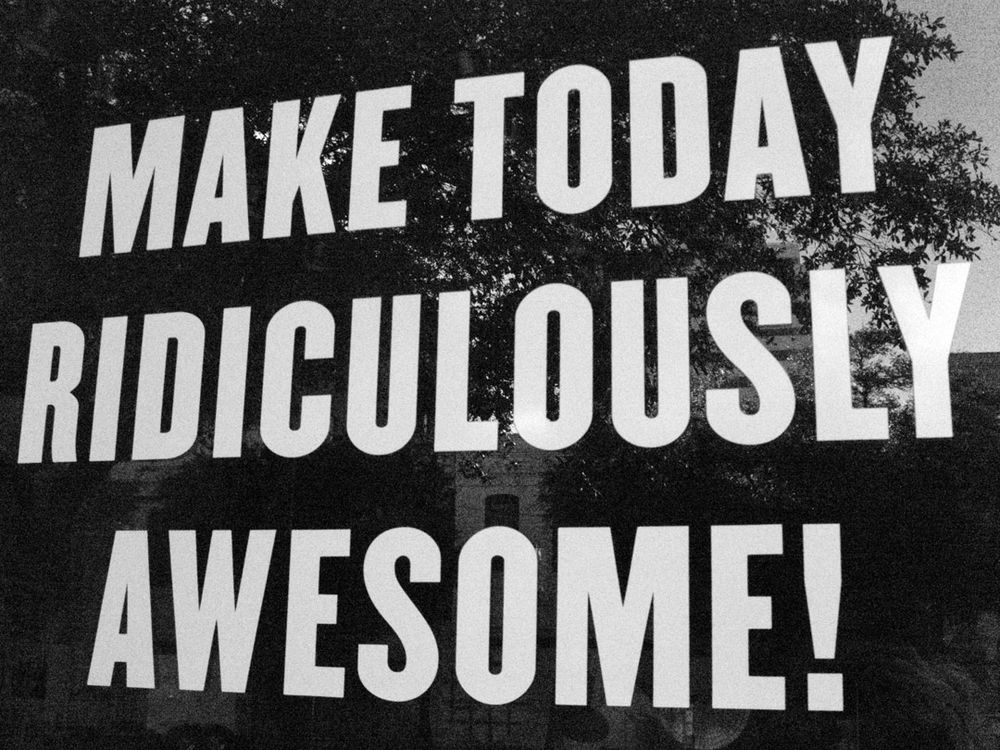 A black and white photograph of a downtown Austin, Texas storefront window that has big block uppercase letters spelling out in thee lines "MAKE TODAY RIDICULOUSLY AWESOME!" There's a tree and some barely visible buildings in the window's reflection.